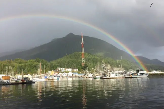 Rainbow over a harbor with boats and a mountain backdrop.